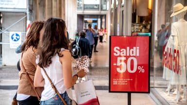 Due donne di spalle che guardano una vetrina con i saldi al 50%